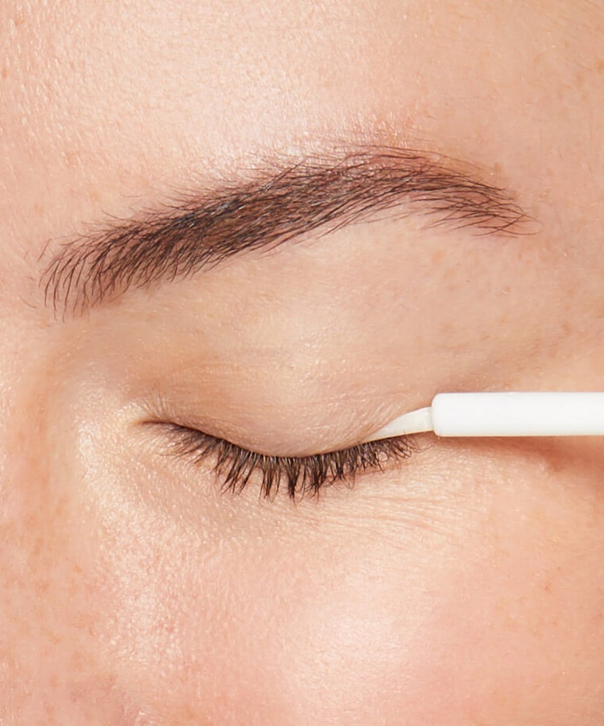 Model uses the white tube of eyelash serum on her eyelash line