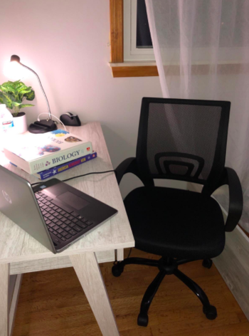 Reviewer's black ergonomic chair next to white wood desk covered in biology books and a laptop