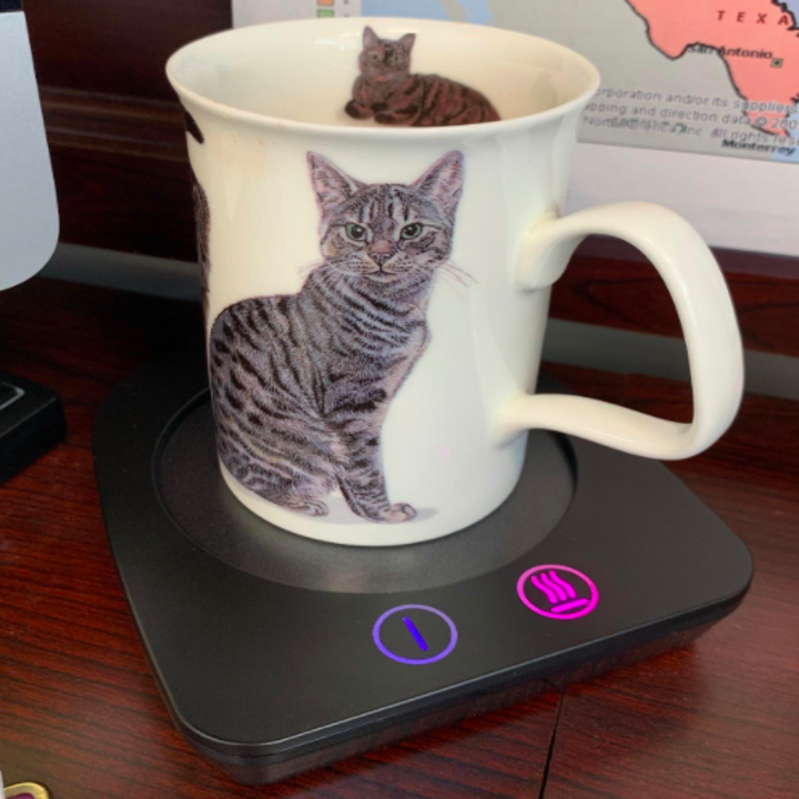 Reviewer uses black mug warmer to heat up cup of coffee with kitty design on front