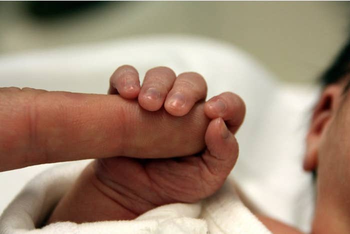 A tiny baby hand holds an adult finger in its palm
