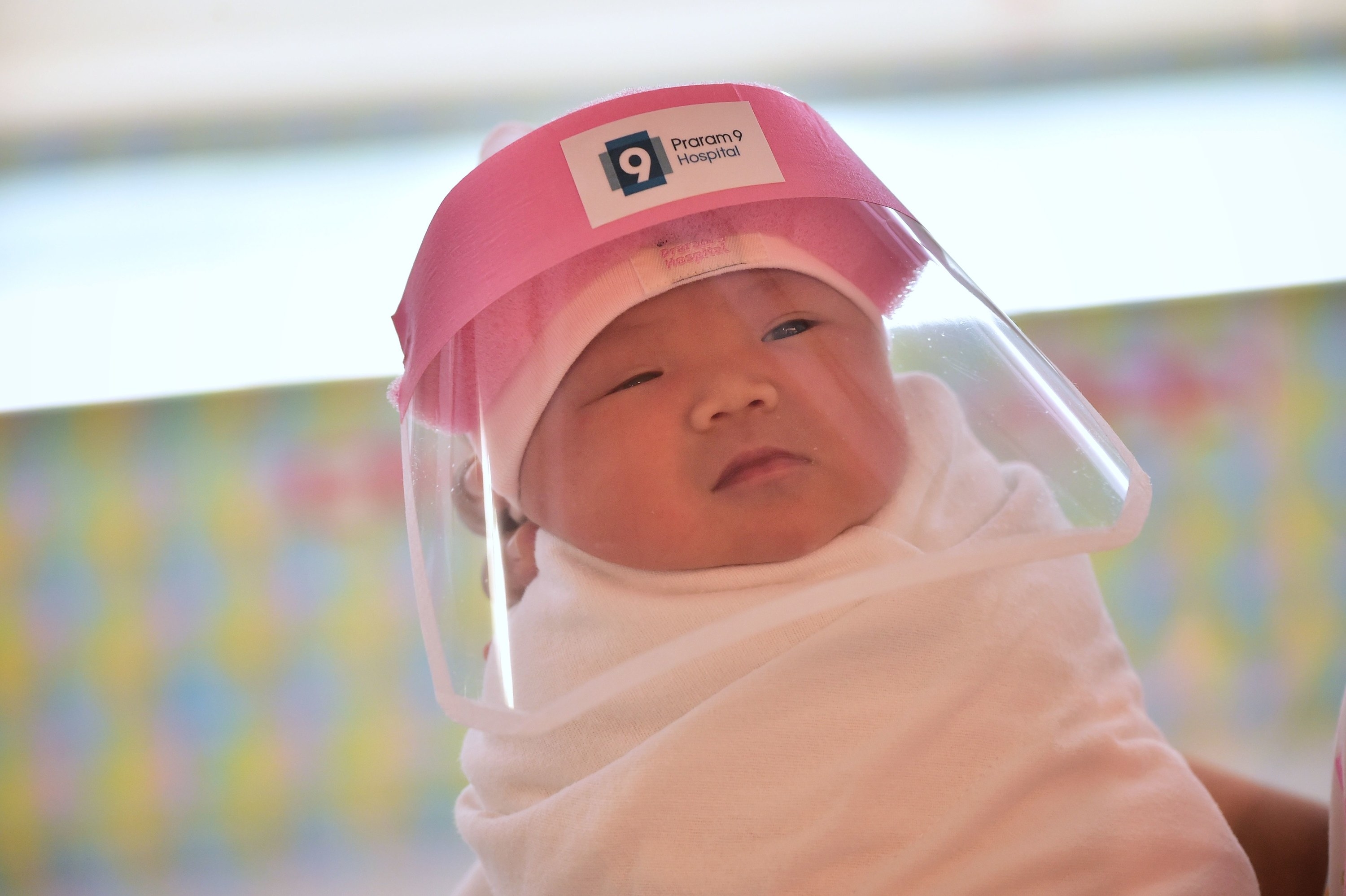 A newborn wears a facial shield