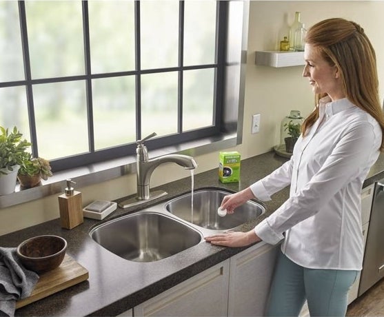 Woman dropping the tablet into a sink-based garbage disposal as water runs from faucet