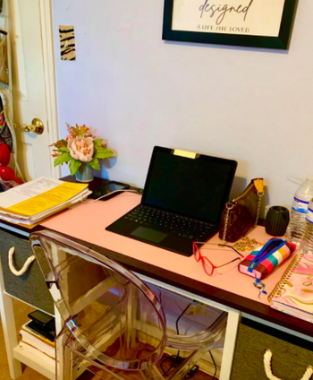 Reviewer uses a light pink desk pad for their black laptop, rainbow pencil case, and other WFH supplies