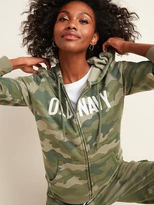 Model wearing the hoodie in green camo color zipped up over a white shirt