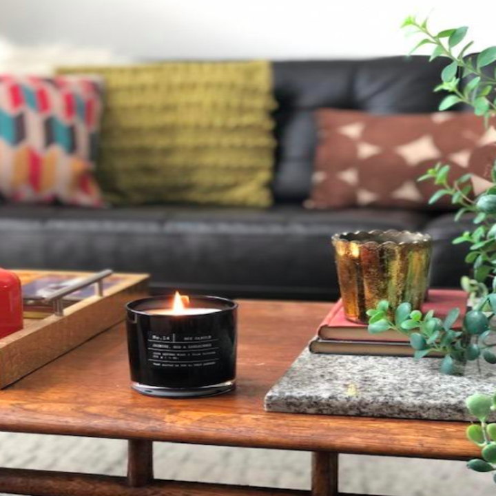 Black candle on top of coffee table covered with a plant, tray, and marble coasters