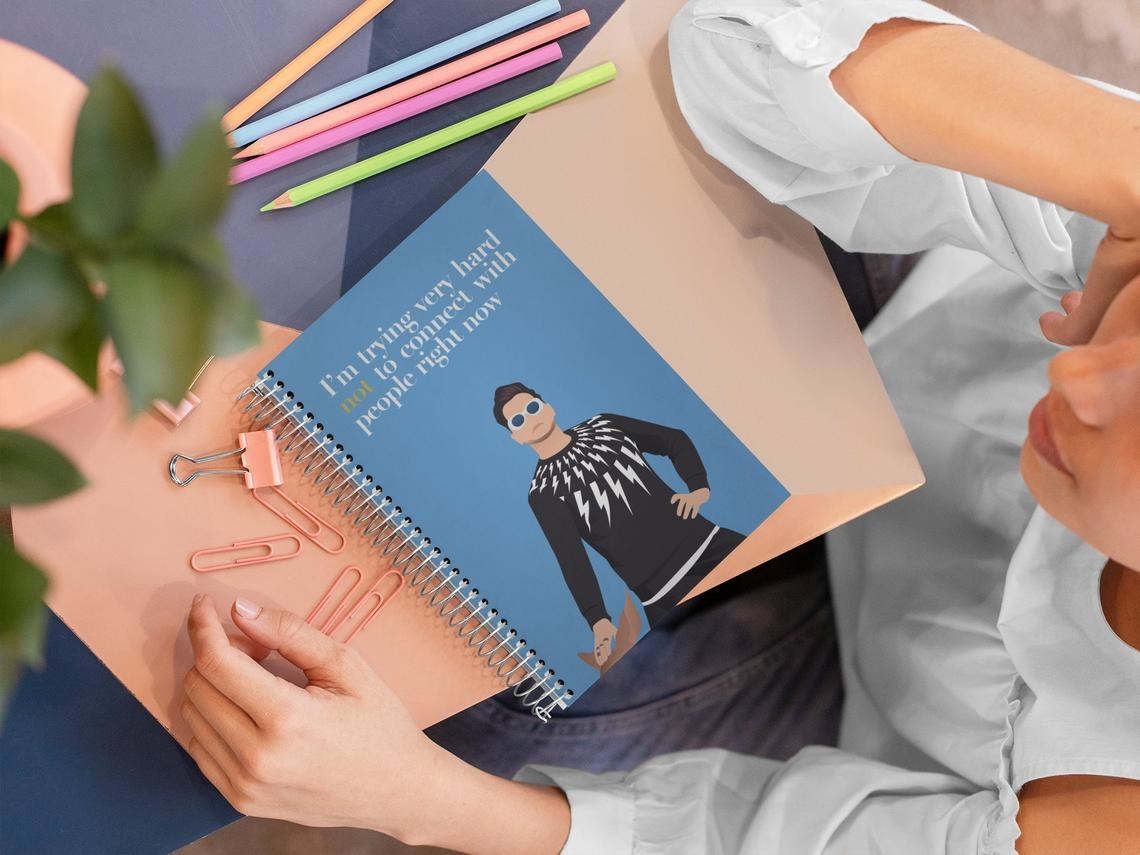 The notebook on a table surrounded by pencil crayons and paper clips
