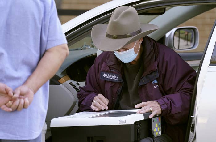 A person sitting in their car fills out a ballot on a touch screen and an election official watches