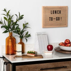 A countertop with vases, cutting board, and brown wooden lazy susan holding a bowl of apples