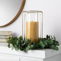 A faux eucalyptus wreath lying on a mantle with a candle in the middle