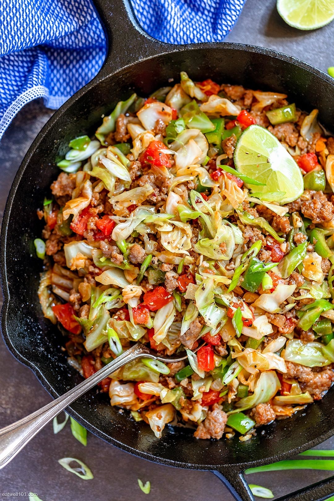 A skillet filled with crumbled sausage, green cabbage, and peppers.