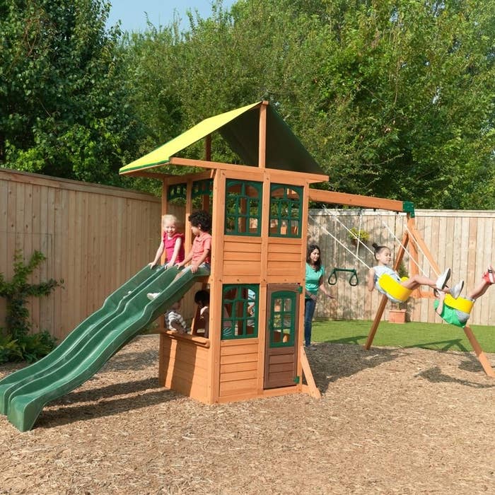 Brown swing set with green slides, roof, and window, and yellow swings