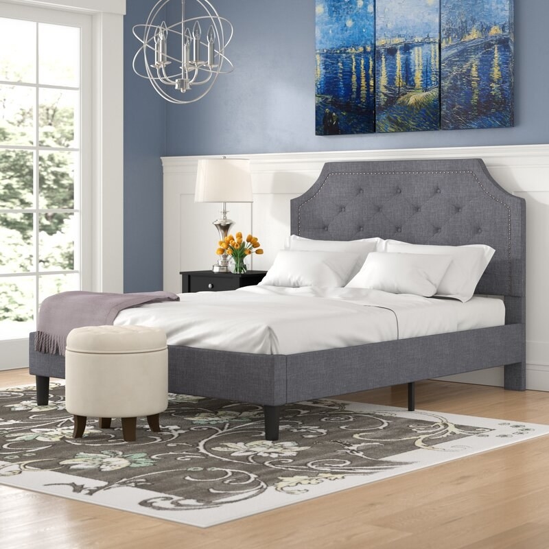 A gray upholstered bed frame with tufted headboard