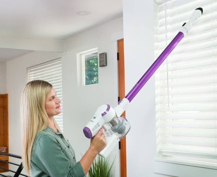 person using a purple cordless lightweight vacuum to clean blinds