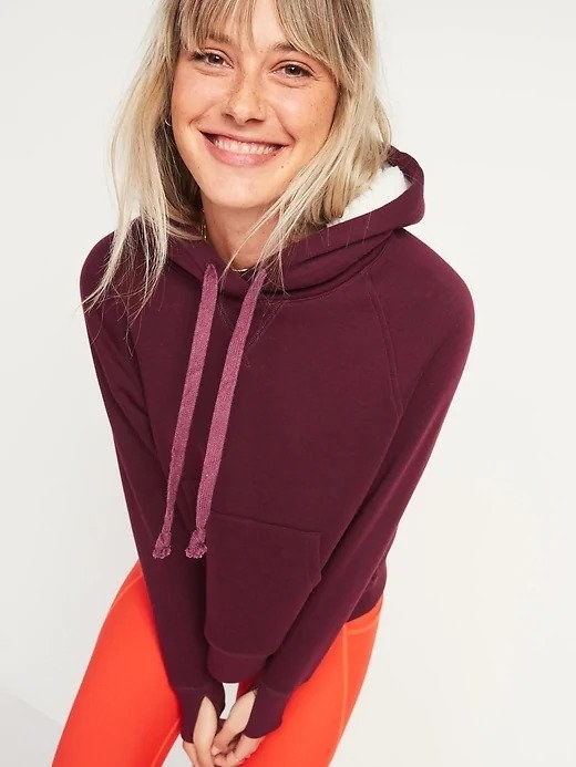 A woman wearing a dark purple pullover hoodie and an orange pair of sweatpants