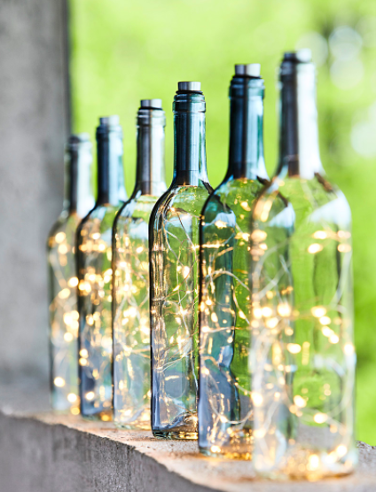 Six glass bottles filled with twinkling lights on a window sill
