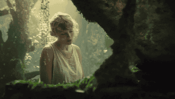 In the woods, Taylor plays on a piano with moss growing on it and water pouring out of it 
