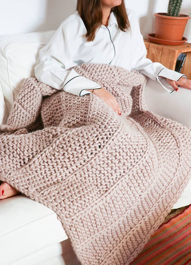 Modl with a large chunky knit blanket in light pink over their lap