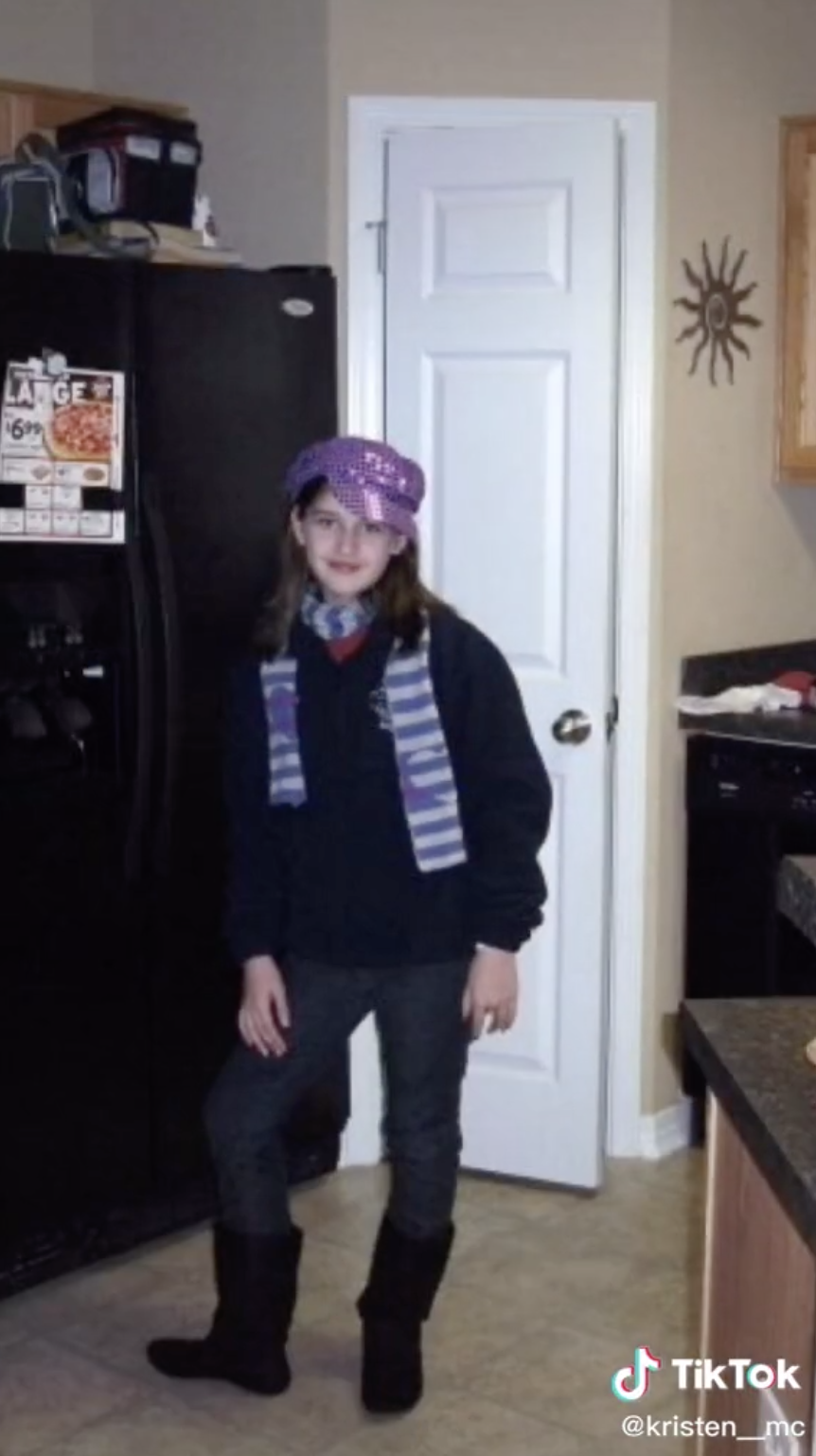 @kris__elise posing in front of a fridge while wearing a bucket hat and a scarf