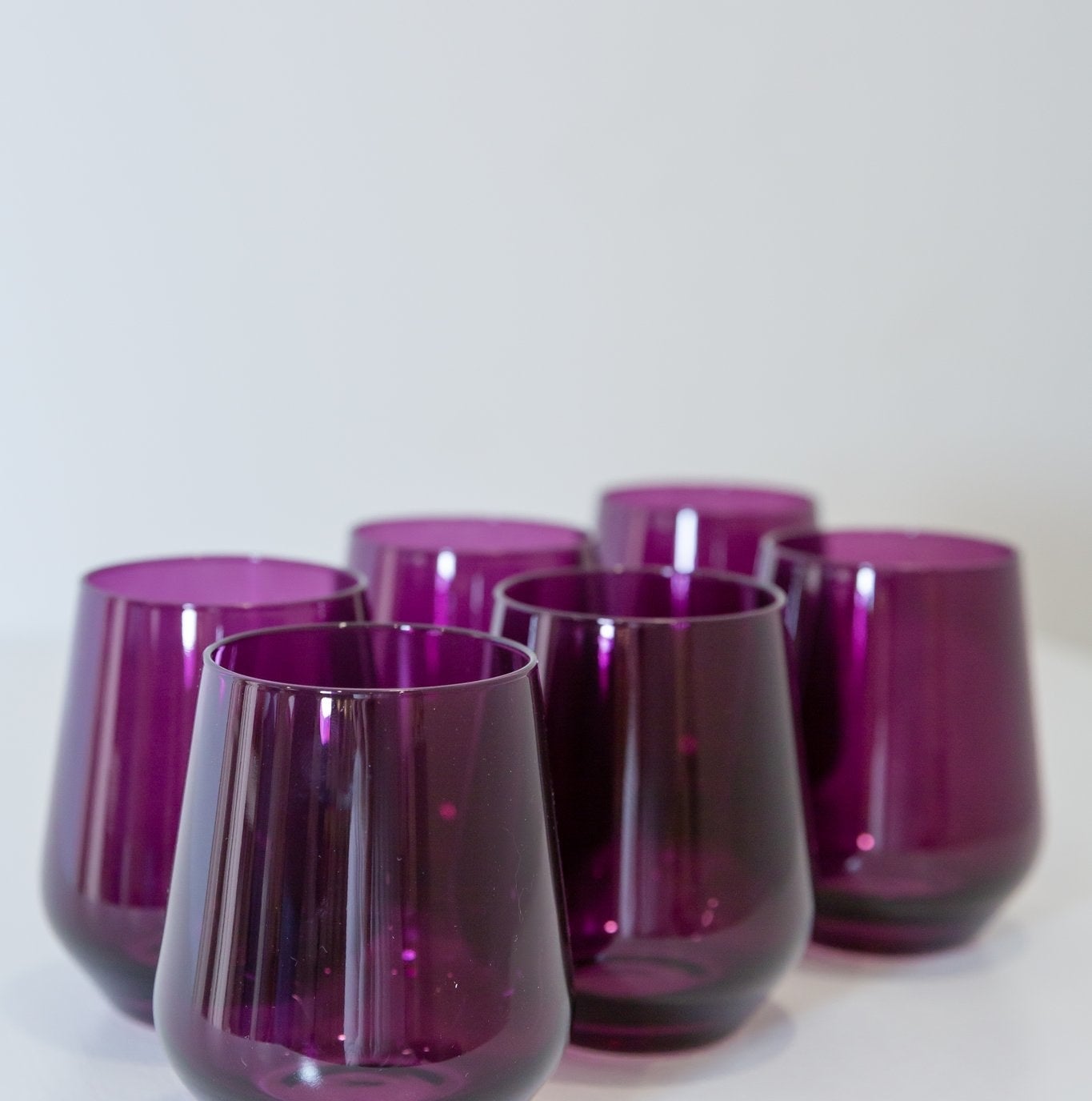 A set of six stemless wine glasses in a dark purple color