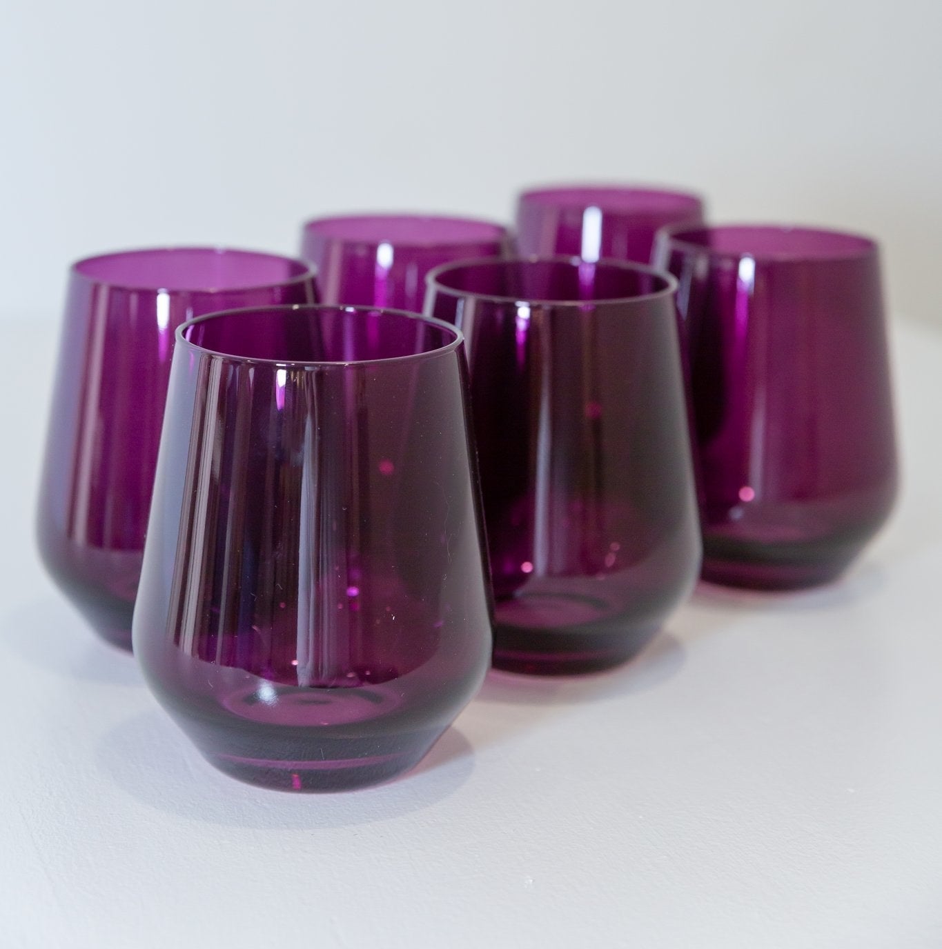 A set of six stemless wine glasses in a dark purple color