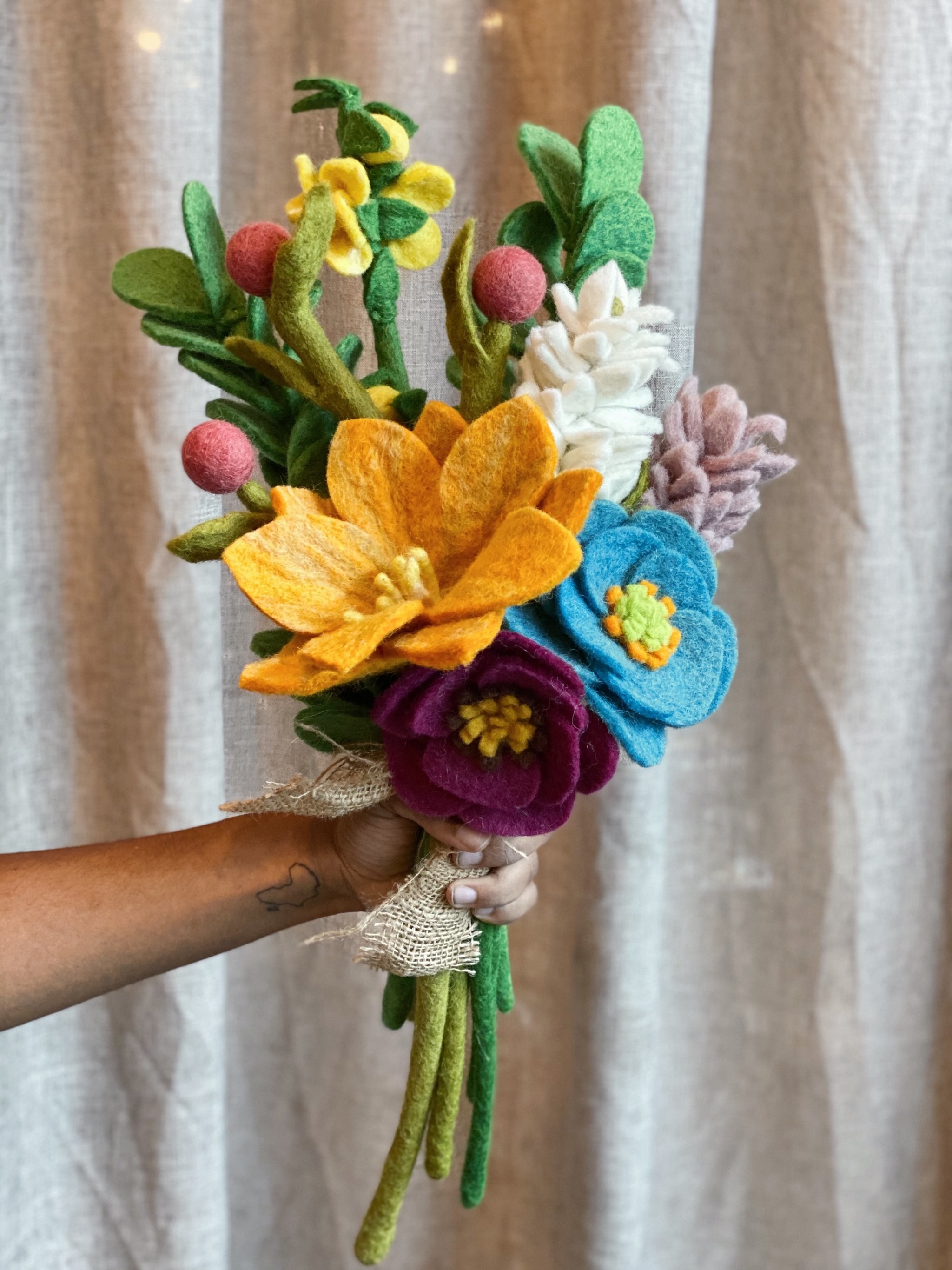 hand holding a bouquet of all different types and colors of flowers made out of felt