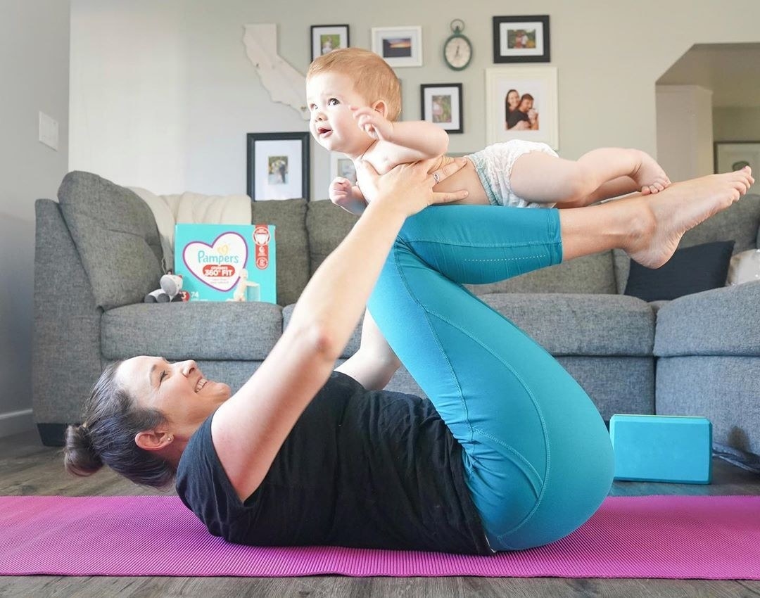 Mother doing yoga pose while holding baby on her legs
