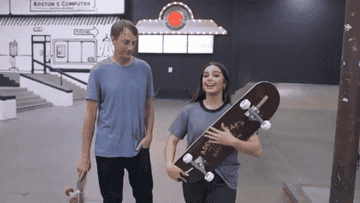 Addison holds a skateboard while pointing to Tony