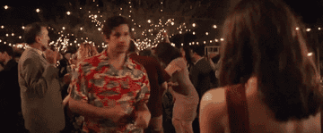 GIF of Andy Samberg on the dance floor at a wedding surrounded by other guests dancing. He is doing funny dances to impress someone.