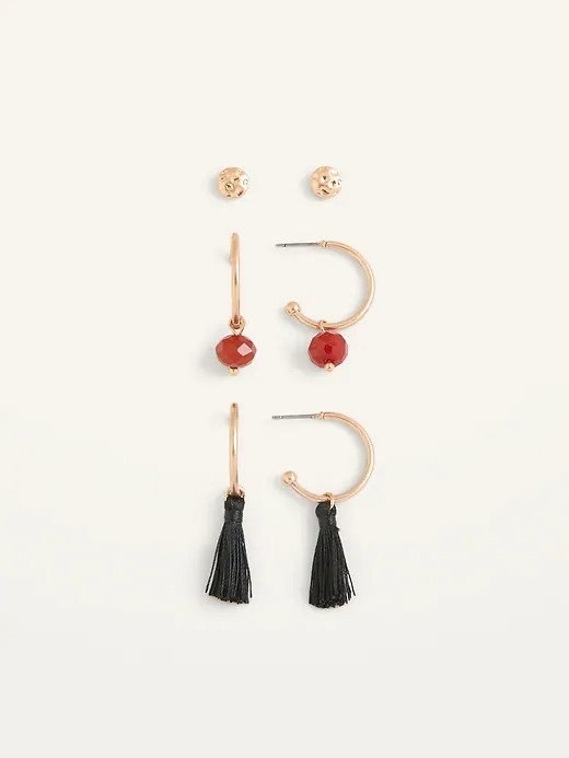 A pair of gold stud earrings displayed above a pair of red stone earrings and a pair of black tassel earrings