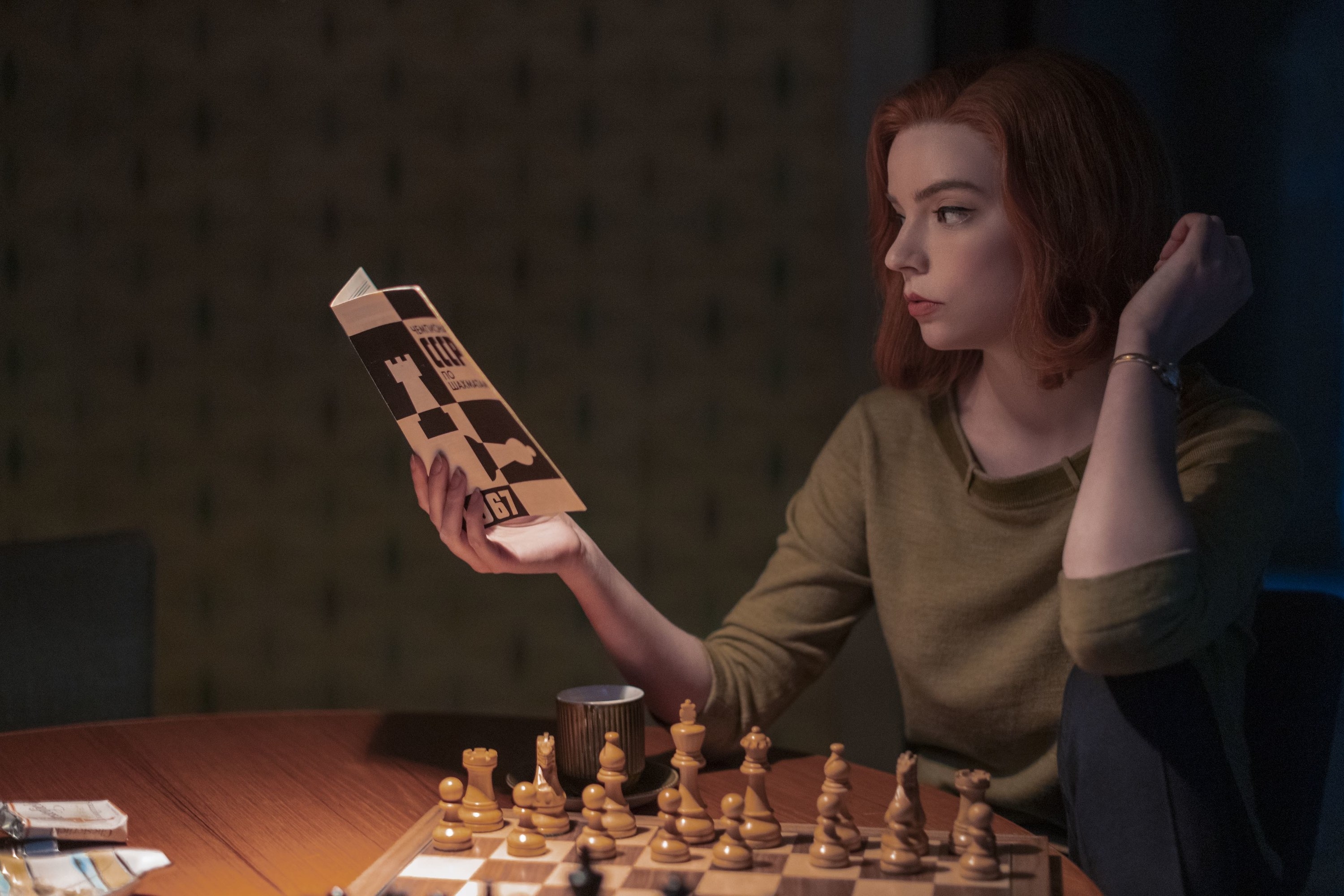 Beth reading a pamphlet while sitting in front a chess board