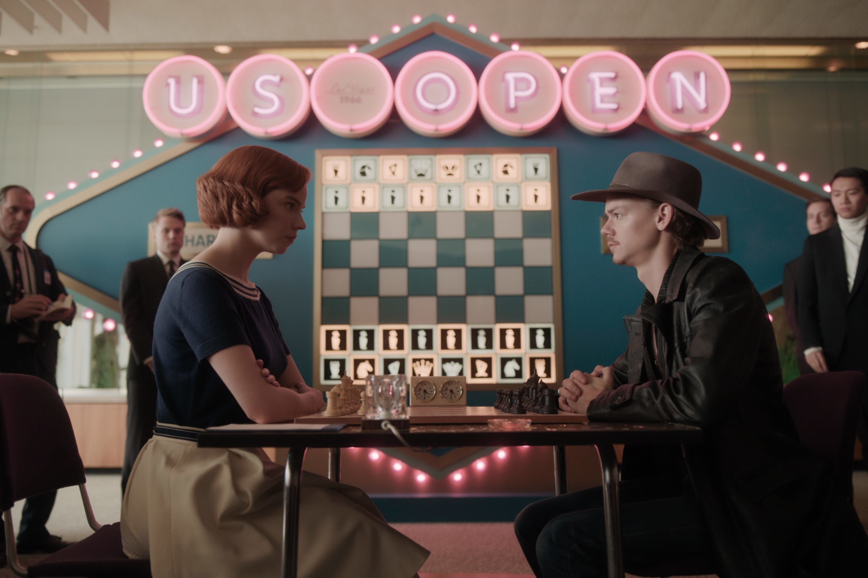 Beth and Benny face off in a chess match as several people watch