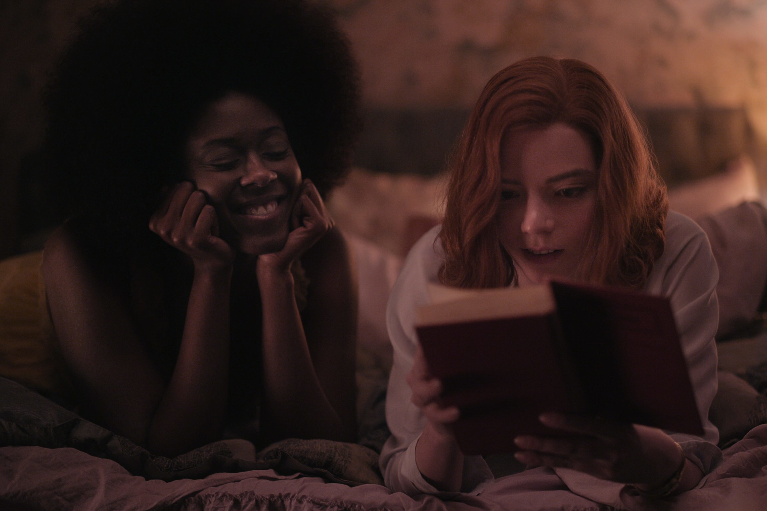 Jolene and Beth laying on a bed as Beth reads a book