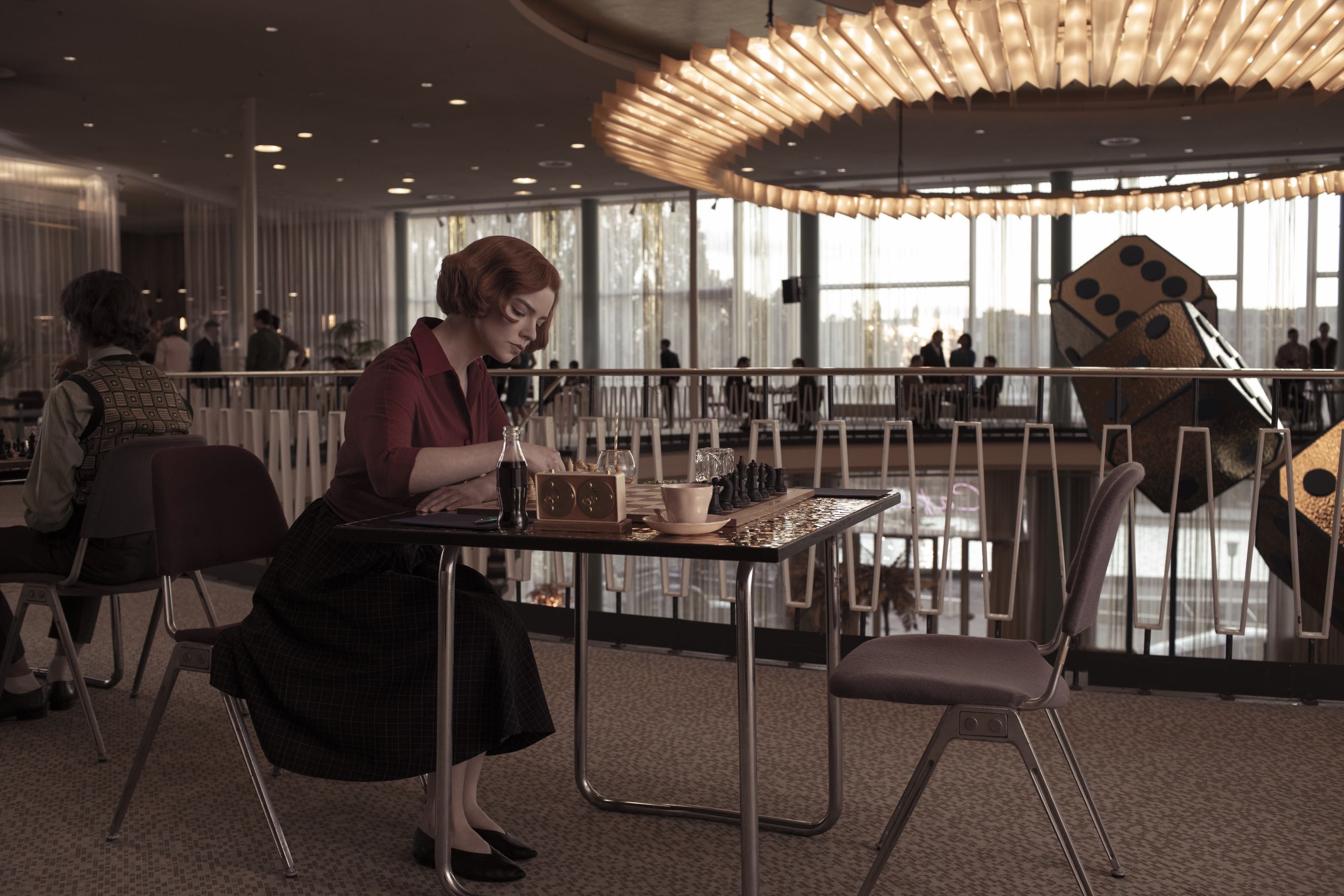 Beth sitting alone at a chess tournament