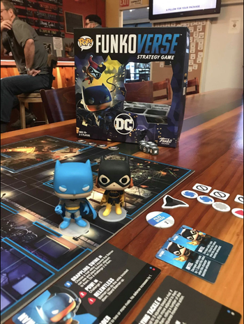 A reviewer photo of the Funkoverse DC Comics board game setup in a restaurant ready to be played