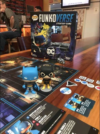 A reviewer photo of the Funkoverse DC Comics board game setup in a restaurant ready to be played
