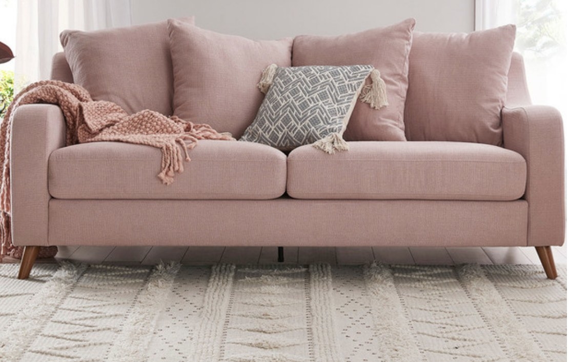 A three seater couch with a pillow and throw blanket