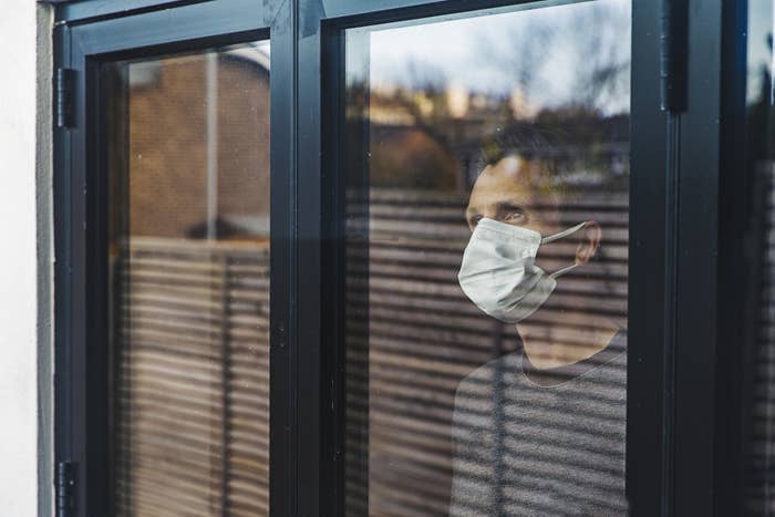 A guy with a mask staring out a window because he's self-isolating.