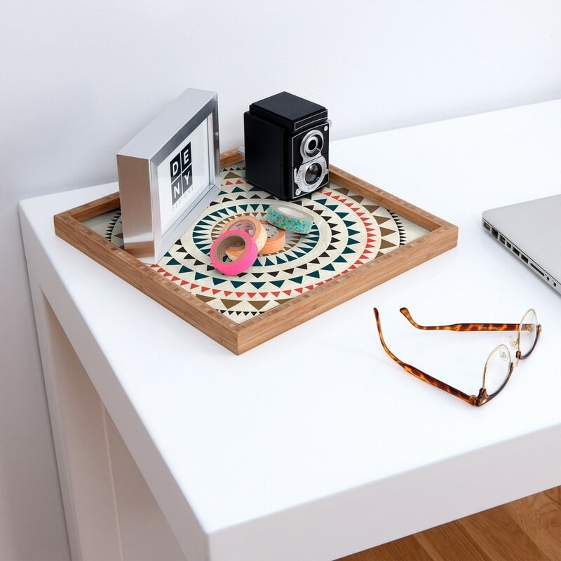 A counter with a geometric tray on it holding a small old school camera, colorful washi tapes and a silver frame