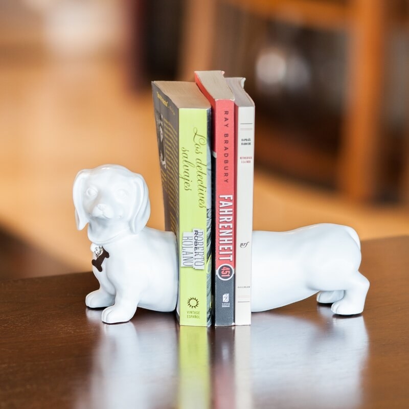 White bookends that look like a dachshund dog with three books in the middle