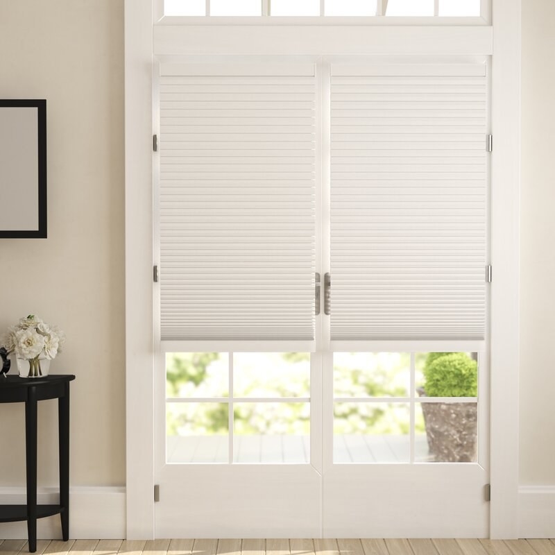 White double doors leading to a backyard with a pair of white honeycomb cell shades halfway open 