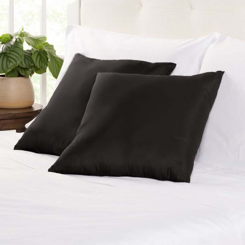 Two small black throw pillows on white bed sheets 