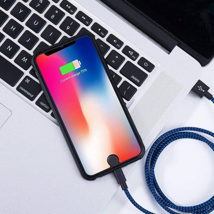 A phone with the cord plugged into it resting on a laptop