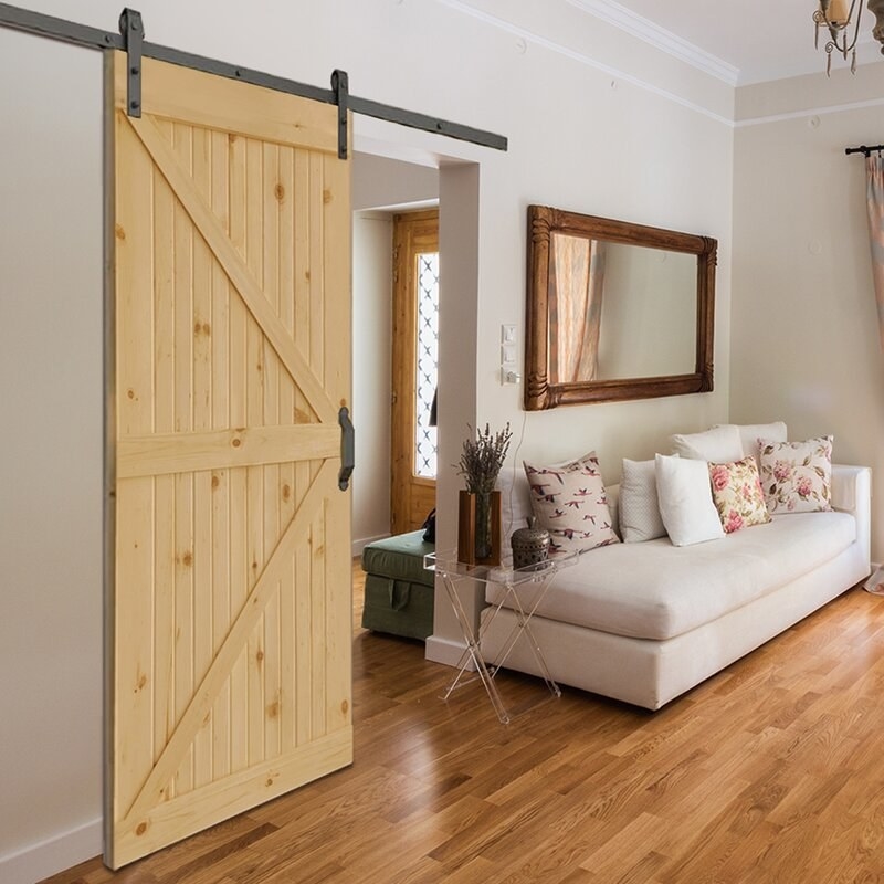 A living room showing a pine wood barn door hanging on a wall next to a chaise lounge and accent mirror