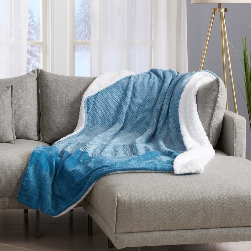 A gray couch with a blue and white velvety throw blanket on it