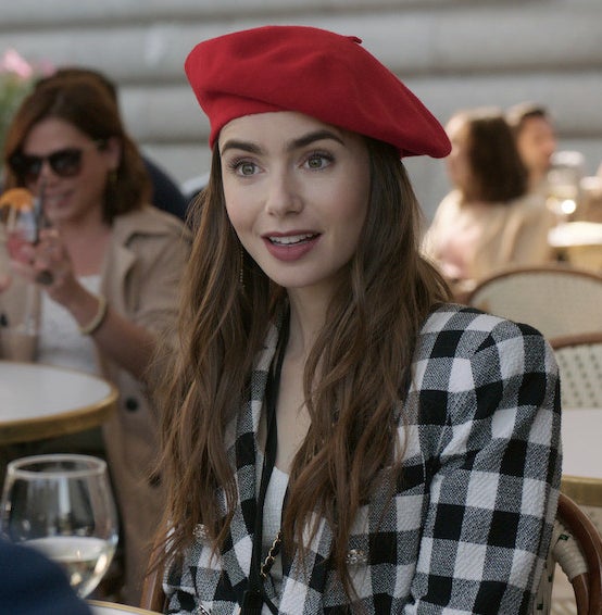 A still of Emily sitting a cafe table and wearing a beret