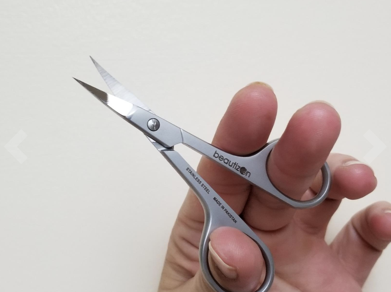 Reviewer holding up tiny stainless steel scissors with curved blades 
