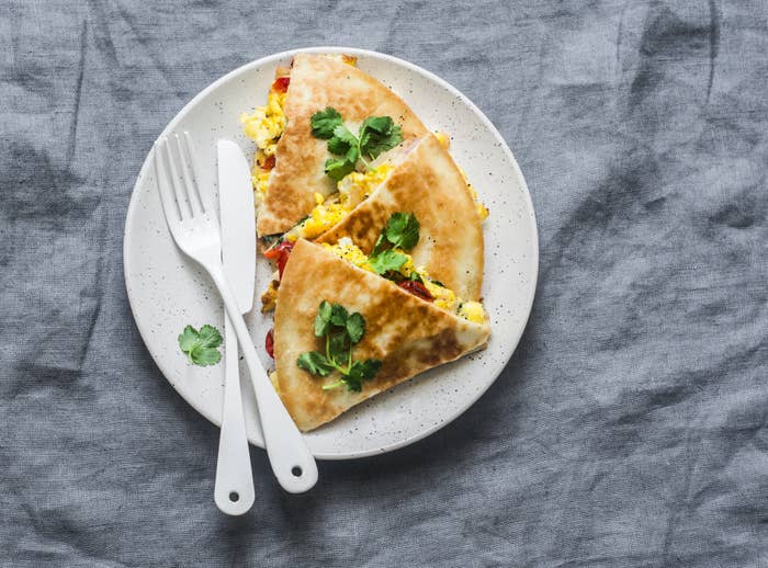 An egg quesadilla with herbs on top, sliced into three triangles. 