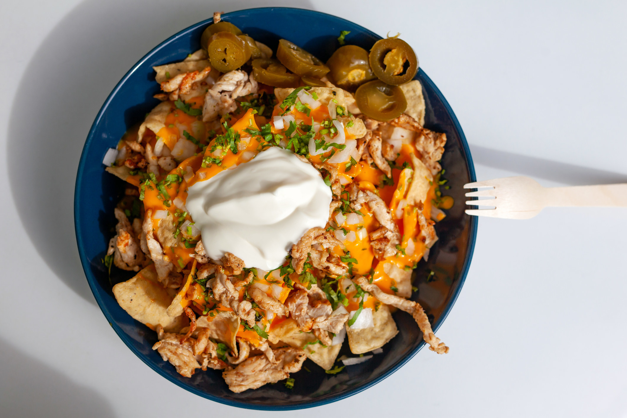 A plate of nachos topped with shredded chicken, melted cheese, herbs, sour cream, and pickled jalapeños. 
