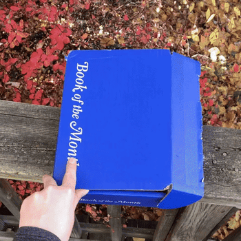gif of a BuzzFeed writer opening a blue Book of the Month box to reveal the book 