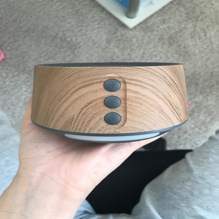 A reviewer holding the white noise machine in wood grain